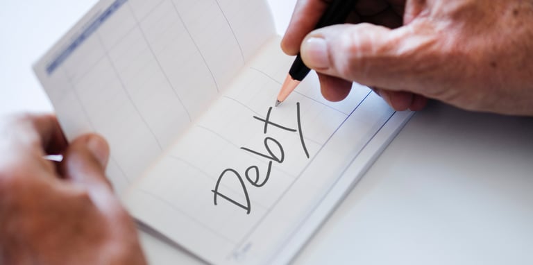 Wrinkled hand writing "debt" with a pen