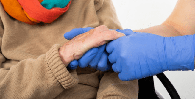 Gloved Caregiver Holding Hands Elderly Woman-1